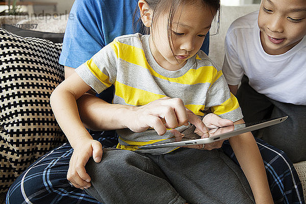 Mittelteil eines Vaters  der seine Tochter anleitet  einen Tablet-Computer zu benutzen  während er mit seinem Sohn auf dem Sofa sitzt