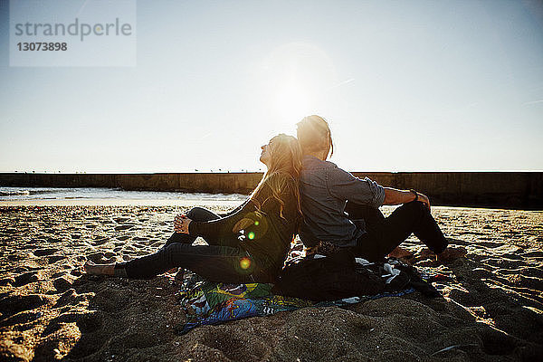 Seitenansicht eines am Strand am Ufer sitzenden Paares bei klarem Himmel