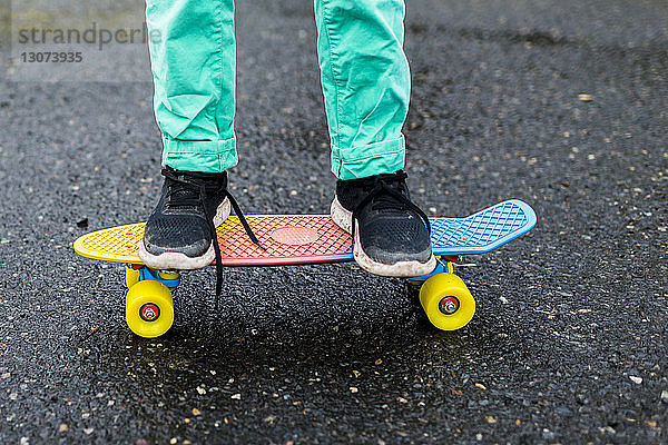 Niedriger Abschnitt eines Jungen beim Skateboarden auf nasser Straße