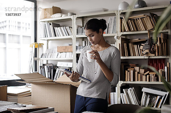 Innenarchitektin hält Kaffeetasse bei Akteneinsicht im Büro