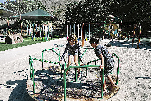 Geschwister spielen auf dem Spielplatz auf einem Karussell