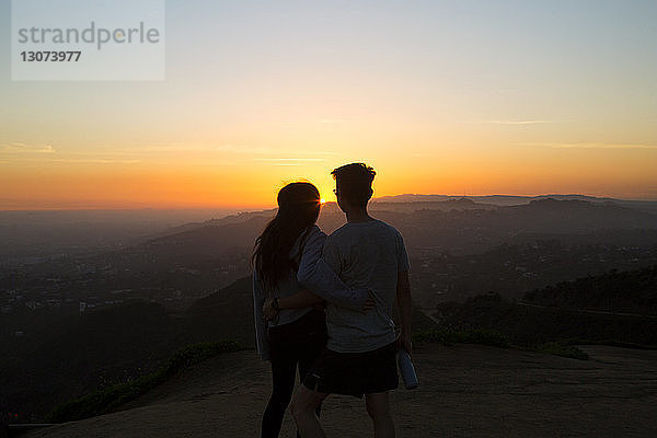 Rückansicht eines Paares  das bei Sonnenuntergang auf einem Berg gegen den Himmel steht