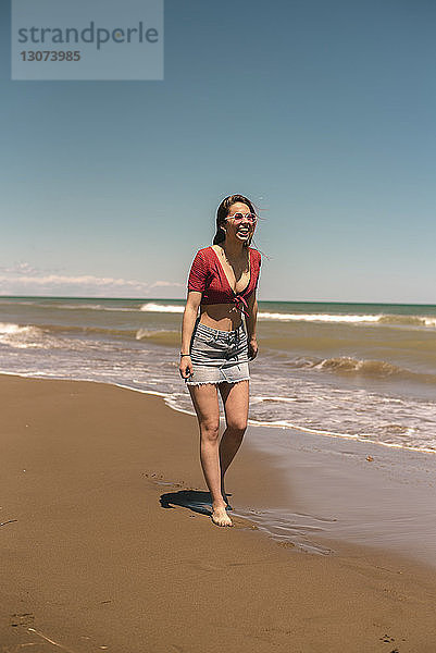 Glückliche Frau geht am Strand gegen blauen Himmel am sonnigen Tag