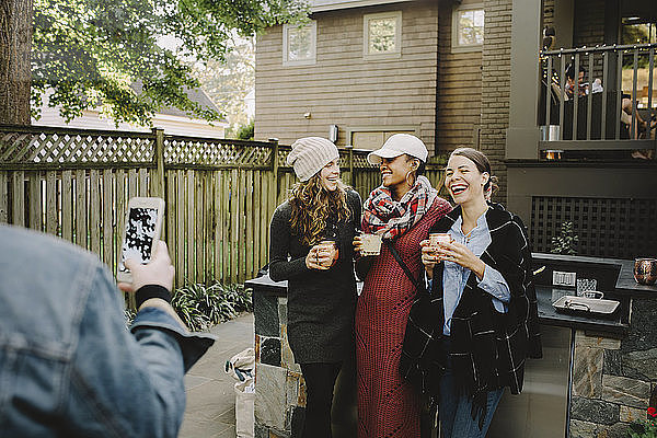 Mann fotografiert Freunde  die Getränke halten  während sie im Hinterhof stehen