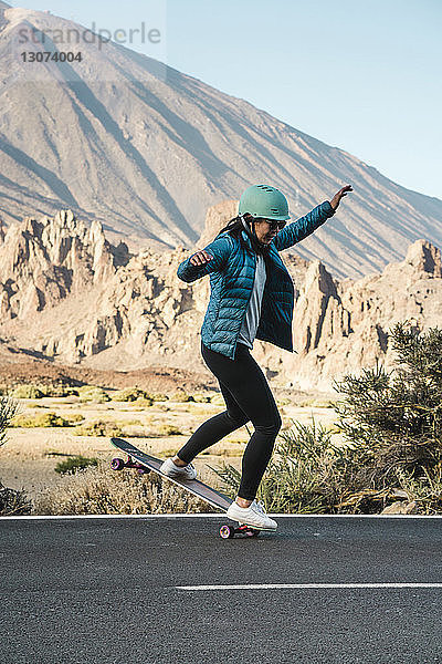 Frau in voller Länge beim Stunt auf Skateboard gegen Berg