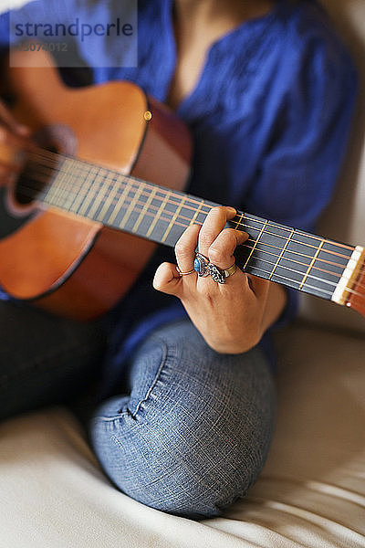 Mittelteil einer Frau  die auf dem Sofa sitzend Gitarre übt