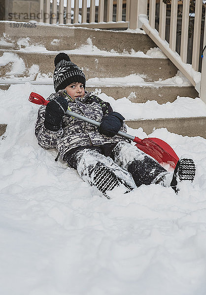 Porträt eines Jungen mit Schaufel auf einer Schneetreppe liegend