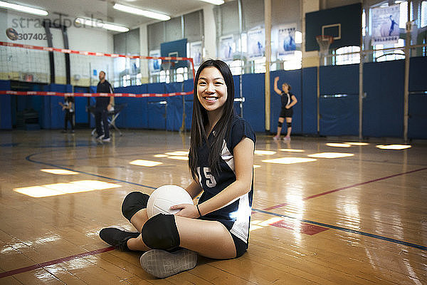 Porträt eines lächelnden Mädchens  das einen Ball hält und auf dem Boden eines Volleyballfeldes sitzt