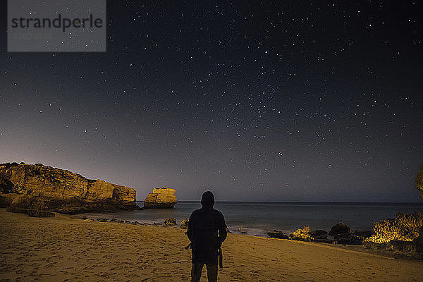 Rückansicht des am Strand stehenden Silhouettenmannes gegen das nächtliche Sternenfeld