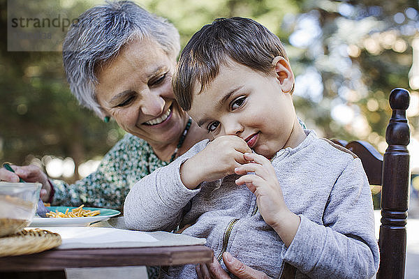 Porträt eines süßen Jungen  der mit der Großmutter an einem Tisch im Freien sitzt