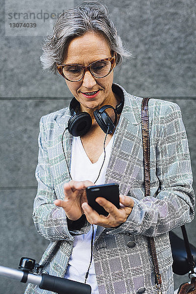 Frau in Jacke benutzt Smartphone  während sie an der Wand steht