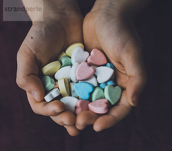 Abgetrennte Hände eines Jungen  der zu Hause bunte Bonbons in Herzform hält