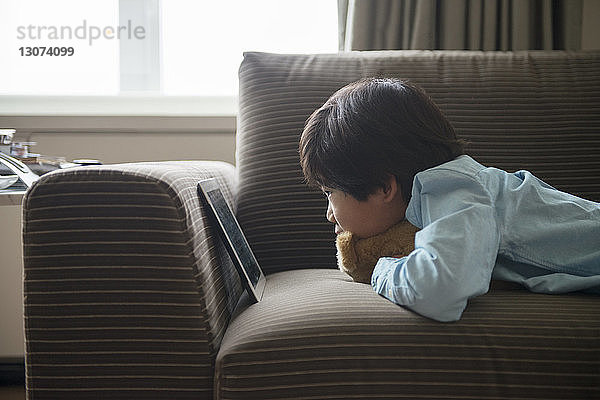 Seitenansicht eines Jungen  der die Tablette betrachtet  während er zu Hause auf dem Sofa liegt