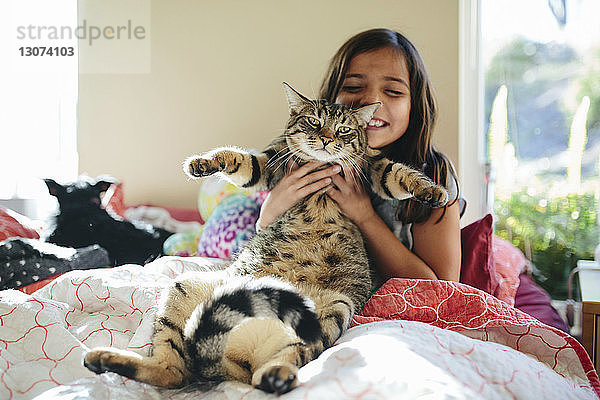 Glückliches Mädchen mit Katze sitzt zu Hause auf dem Bett