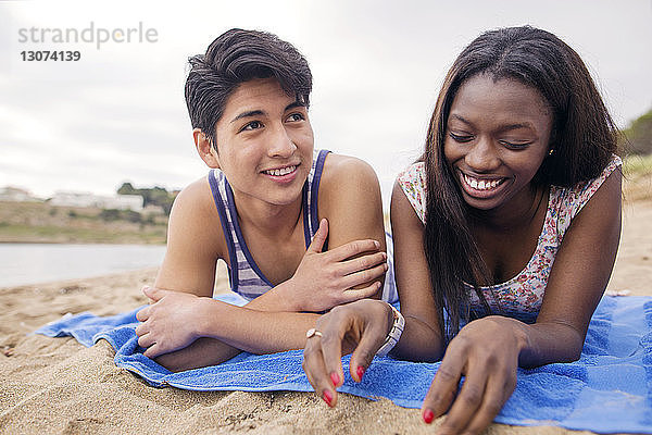 Glückliches multiethnisches Paar liegt auf einer Decke am Strand