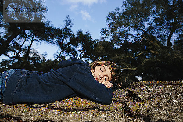 Niedrigwinkelansicht eines auf einem Baumstamm schlafenden Mädchens im Wald