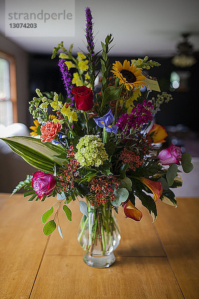 Verschiedene Blumen in Glasvase auf Holztisch zu Hause