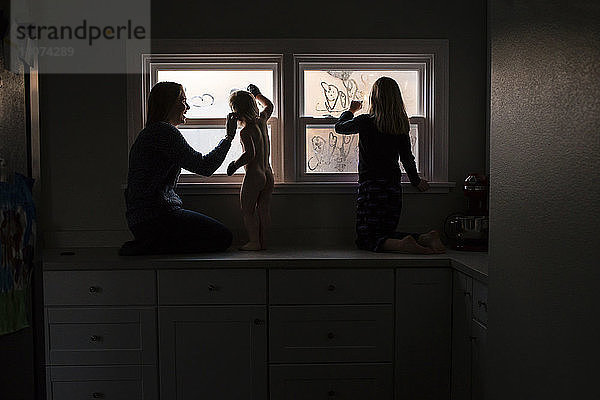 Glückliche Mutter sieht Kinder an  die am Fenster in der Küche Herzform machen