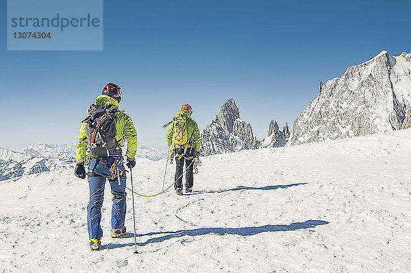 Rückansicht von Wanderern mit Seil  die auf einem schneebedeckten Berg bei strahlend blauem Himmel gehen