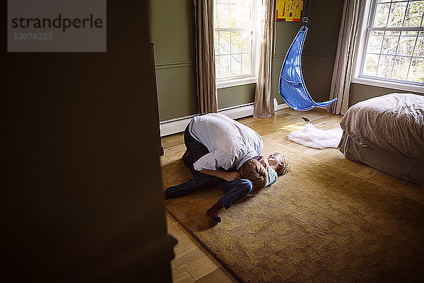 Hochwinkelansicht eines Vaters  der mit seinem glücklichen Sohn auf dem Boden im Schlafzimmer spielt