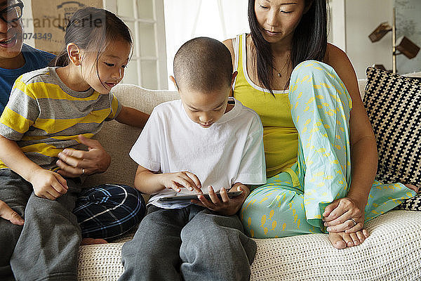 Familie sieht Jungen am Tablet-Computer an  während er zu Hause auf dem Sofa sitzt