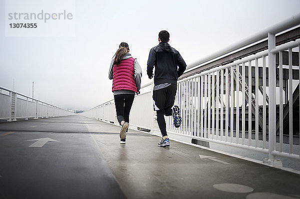 Rückansicht von Athleten  die auf der Bay Bridge gegen den Himmel laufen