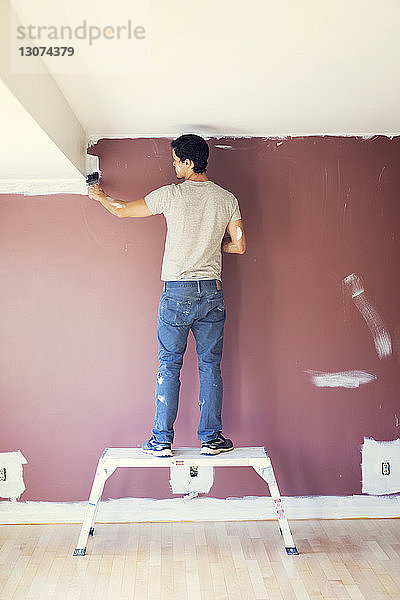 Rückansicht eines Mannes  der zu Hause eine Wand malt