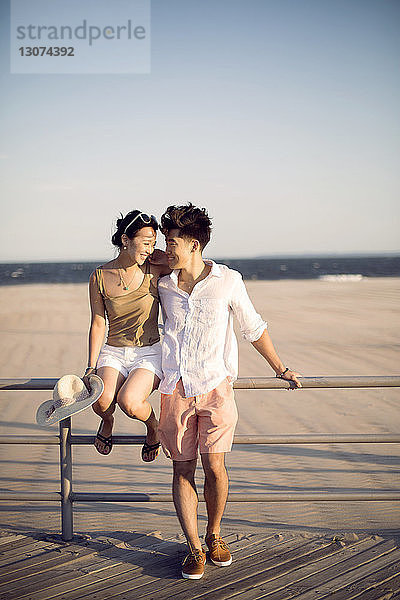 Lächelndes Paar an der Reling am Pier vor klarem Himmel