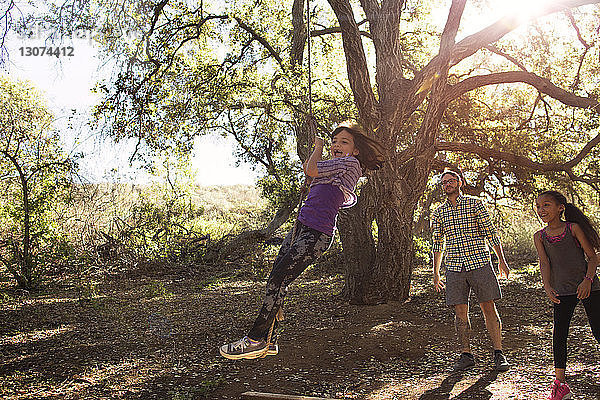 Familie betrachtet fröhliches Mädchen beim Seilschaukeln im Wald