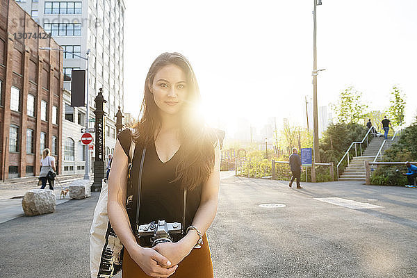 Porträt einer jungen Frau mit Kamera auf der Straße in der Stadt vor klarem Himmel