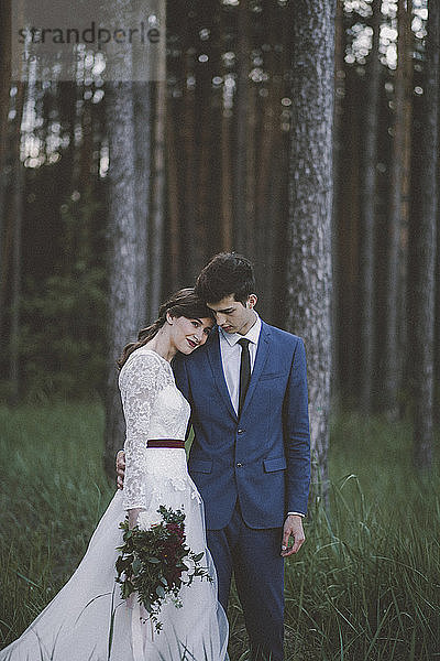 Braut mit Bräutigam auf Grasfeld im Wald stehend