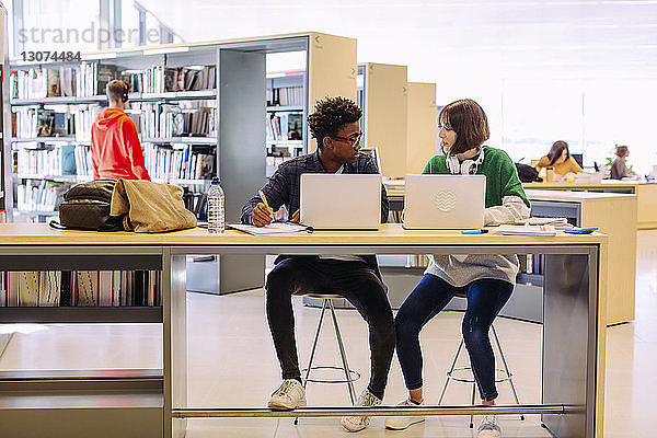 Freunde diskutieren während des Studiums über Laptop-Computer in der Bibliothek