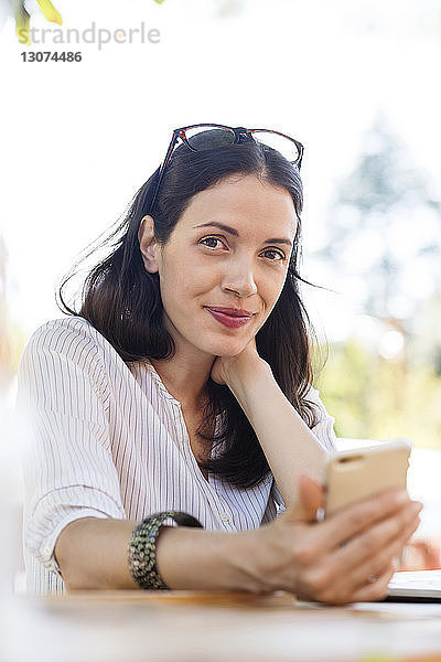 Porträt einer selbstbewussten Frau  die ein Smartphone in der Hand hält  während sie im Straßencafé sitzt