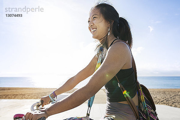 Seitenansicht einer glücklichen sportlichen Frau beim Fahrradfahren am Strand