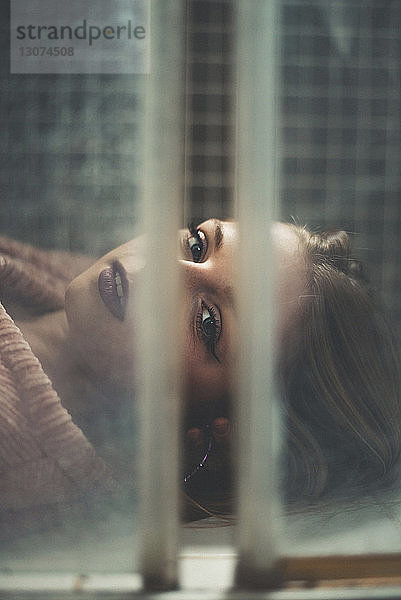 Nahaufnahme einer Frau  die durch ein Fenster schaut  während sie auf einer Kachel liegt