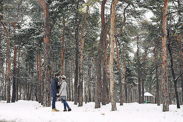 Glückliches Paar sieht sich an  während es auf einem verschneiten Feld im Wald steht