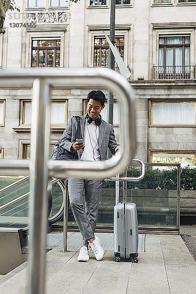 Geschäftsmann mit Gepäck benutzt Smartphone  während er an der Rolltreppe steht