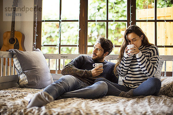 Ehepaar trinkt Kaffee  während es zu Hause auf einem Fensterplatz in einer Nische sitzt