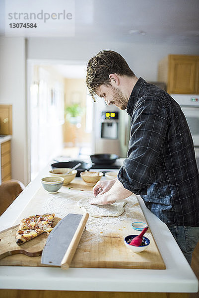 Seitenansicht eines Mannes  der zu Hause auf einer Kücheninsel Pizzateig knetet