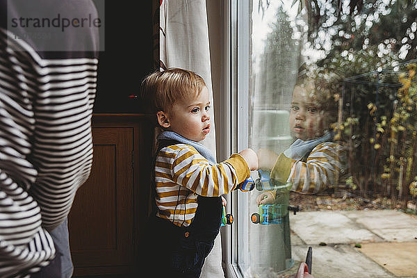 Süßer Sohn schaut zu Hause durch das Fenster der Mutter