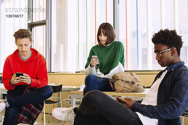 Studenten  die Mobiltelefone benutzen  während sie in der Bibliothek sitzen