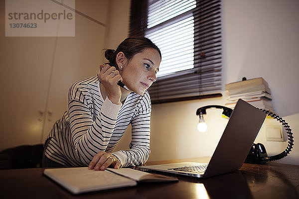 Am Laptop arbeitende Frau an Schreibtischlampe am Tisch