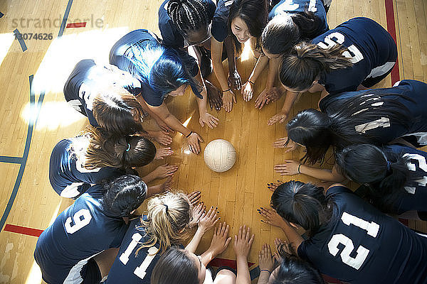 Hochwinkelansicht einer weiblichen Volleyballmannschaft  die auf dem Boden kauert