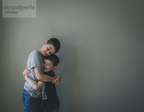 Lächelnde Brüder umarmen sich  während sie zu Hause an der Wand stehen