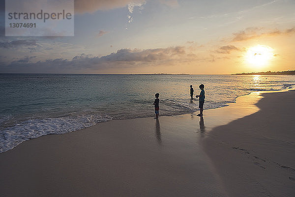 Scherenschnitt-Jungen stehen am Strand am Ufer gegen den Himmel