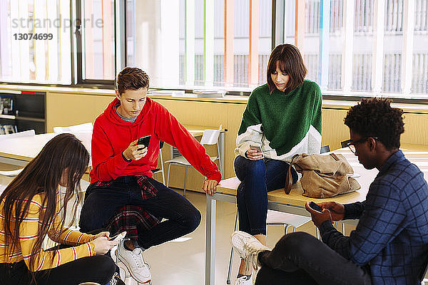 Schülerinnen und Schüler benutzen Smartphones  während sie in der Bibliothek sitzen