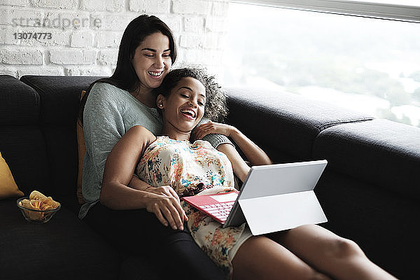 Glückliches lesbisches Paar schaut sich Videos über einen Laptop an  während es sich auf dem Sofa im Wohnzimmer entspannt