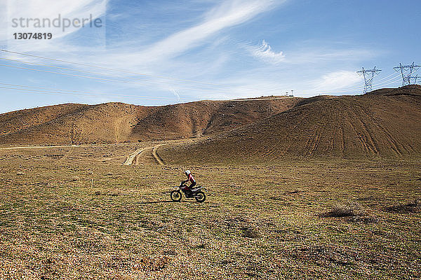 Mitteldistanzansicht einer Motorrad fahrenden Frau auf Landschaft gegen Himmel
