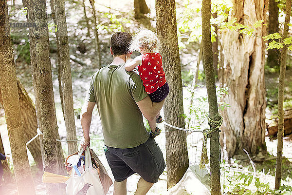 Hochwinkelaufnahme eines Vaters  der seine Tochter und Taschen trägt  während er im Wald spazieren geht