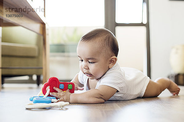Kleiner Junge spielt mit Spielzeug  während er zu Hause auf dem Boden liegt